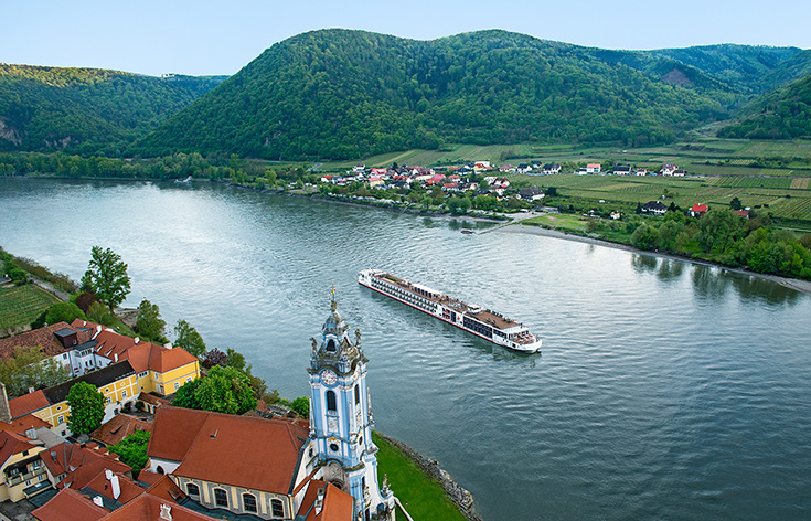 Aerial view of a Viking river ship sailing past a European town